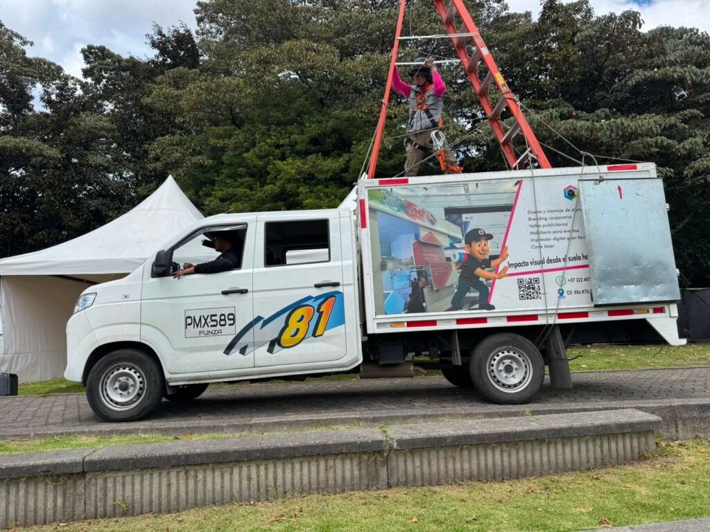 Técnico de BRA Publicidad realizando el montaje de una estructura publicitaria desde un camión de trabajo utilizando arnés, casco y sistema de protección para trabajo seguro en alturas.