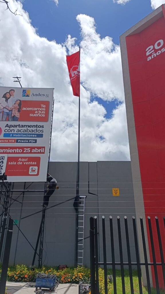 Técnico de BRA Publicidad instalando una valla publicitaria y una bandera corporativa de gran formato mediante trabajo seguro en alturas con equipos de protección certificados.